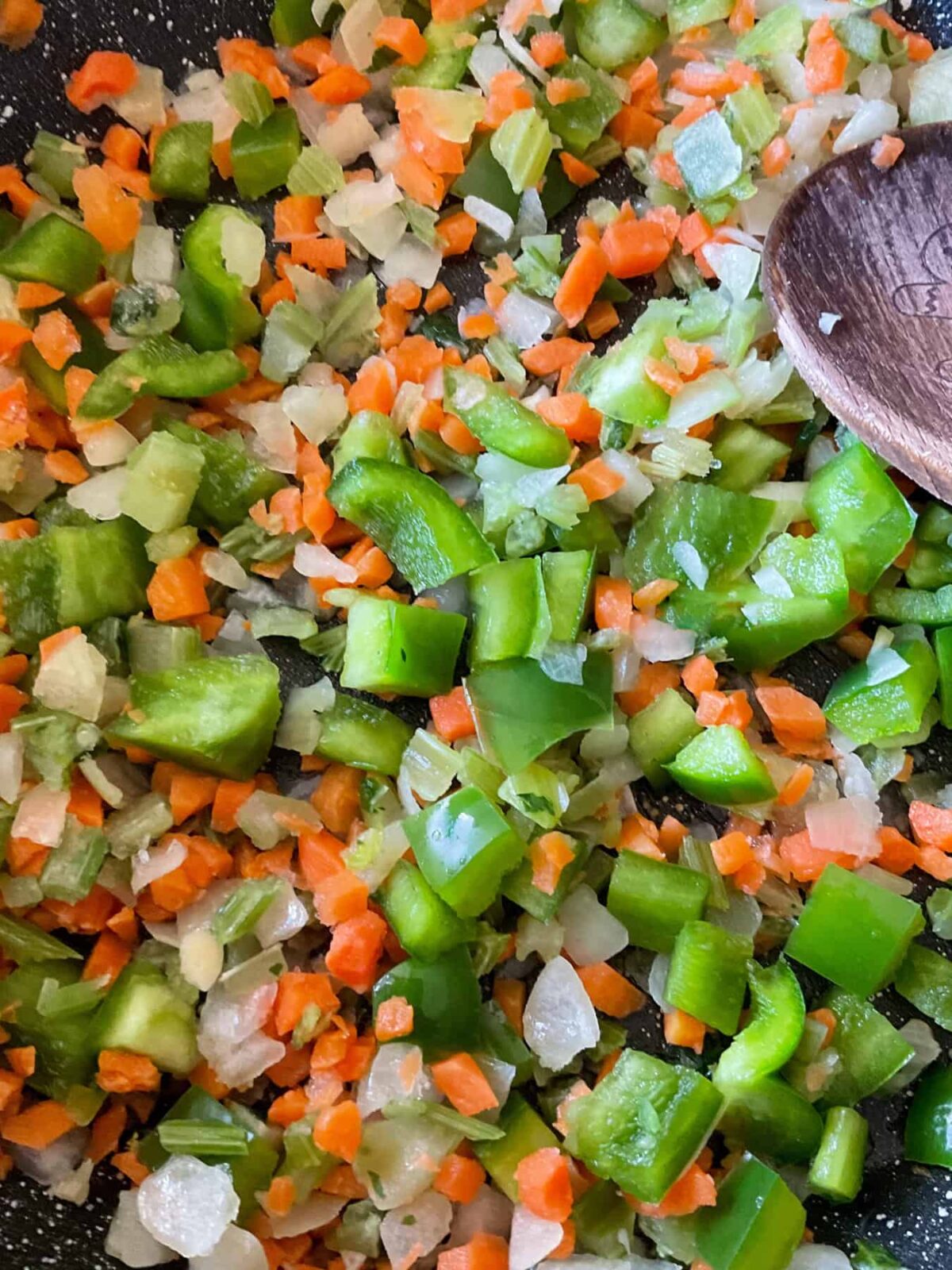 Veggies sauteing in skillet with wooden spoon.