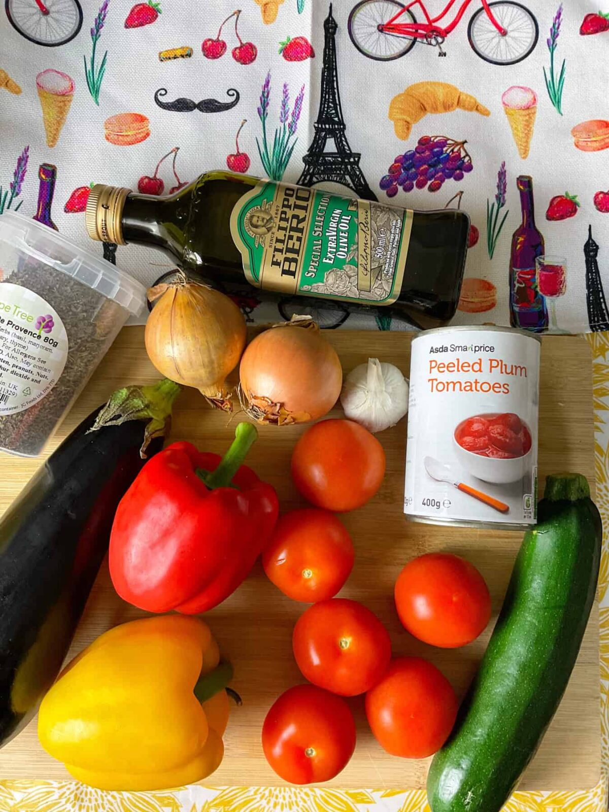 Ingredients for ratatouille on a cutting board with a table mat with images depicting French culture.