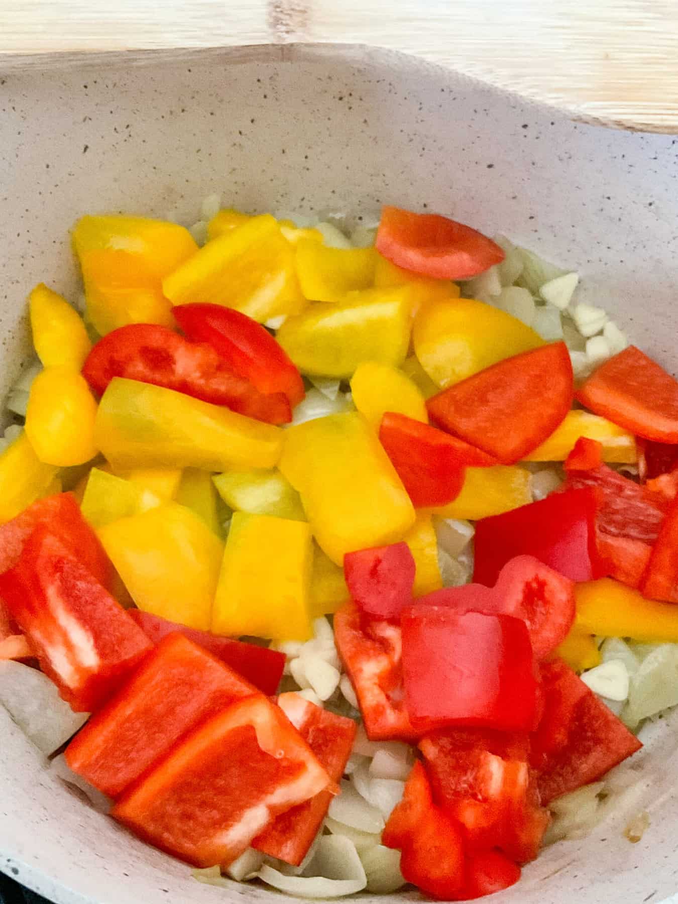 Bell peppers added to onions in stew pot.