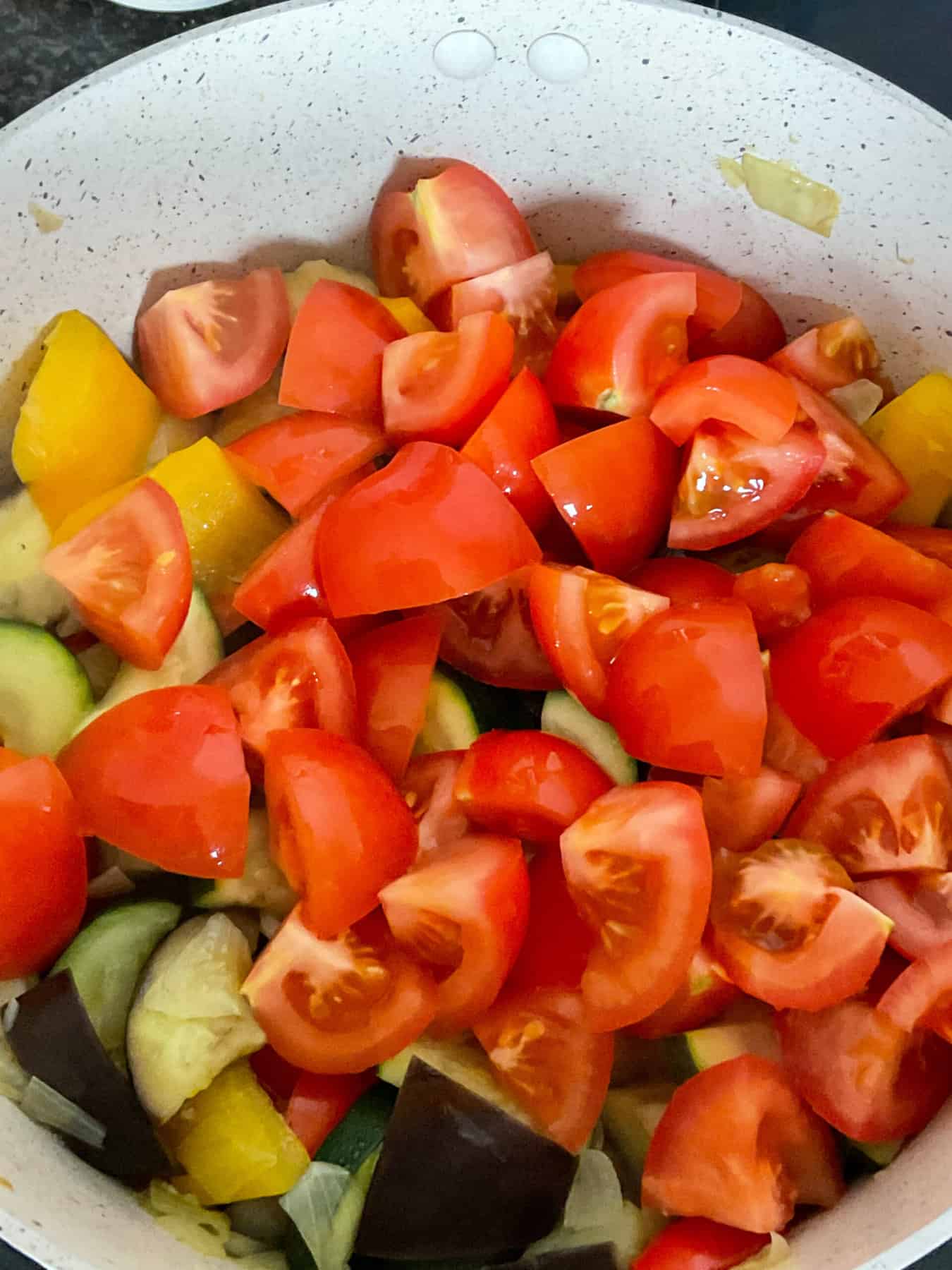 Fresh chopped tomatoes added to ratatouille cooking in stew pot.