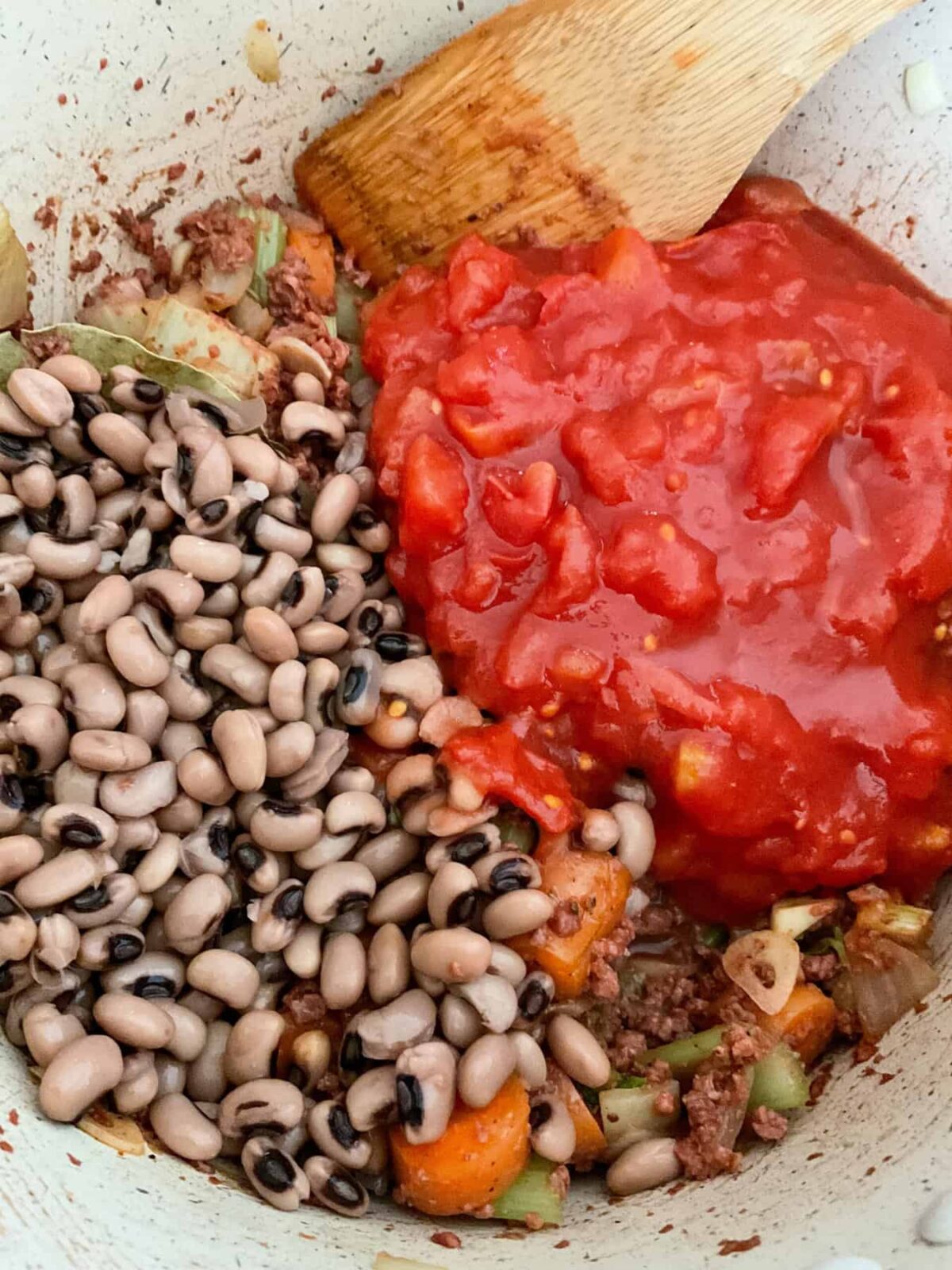 Black eyed beans and canned tomatoes added to ingredients in stew pot.