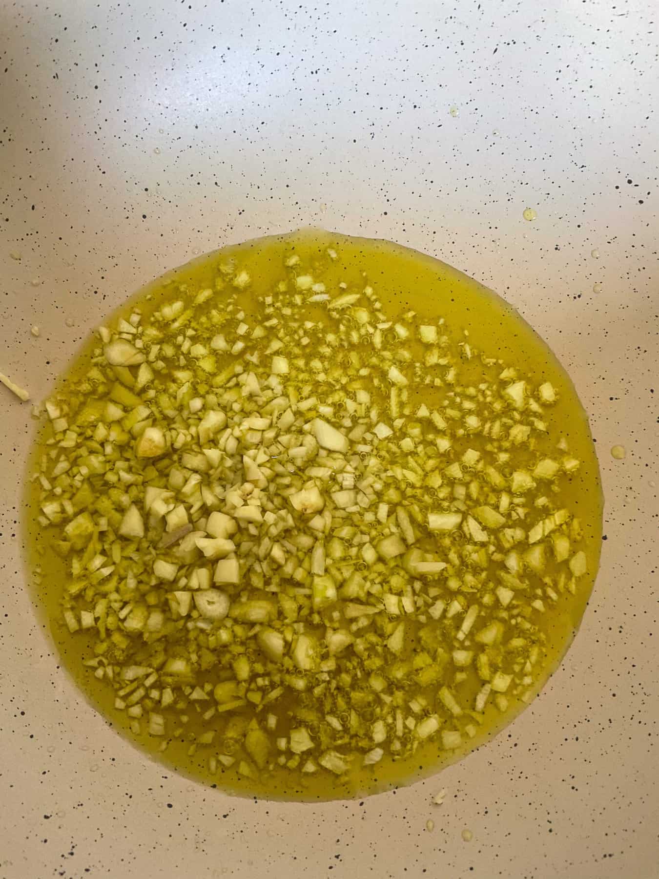 Garlic and olive oil cooking in cream coloured large fry pan.