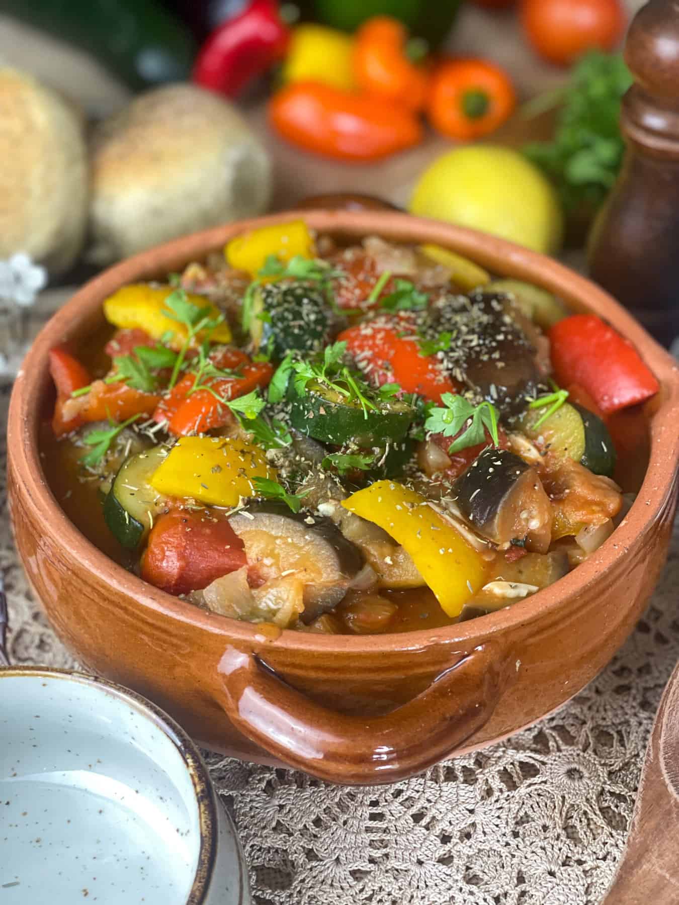 A serving bowl of ratatouille garnished with dried and fresh herbs and empty bowl in front.