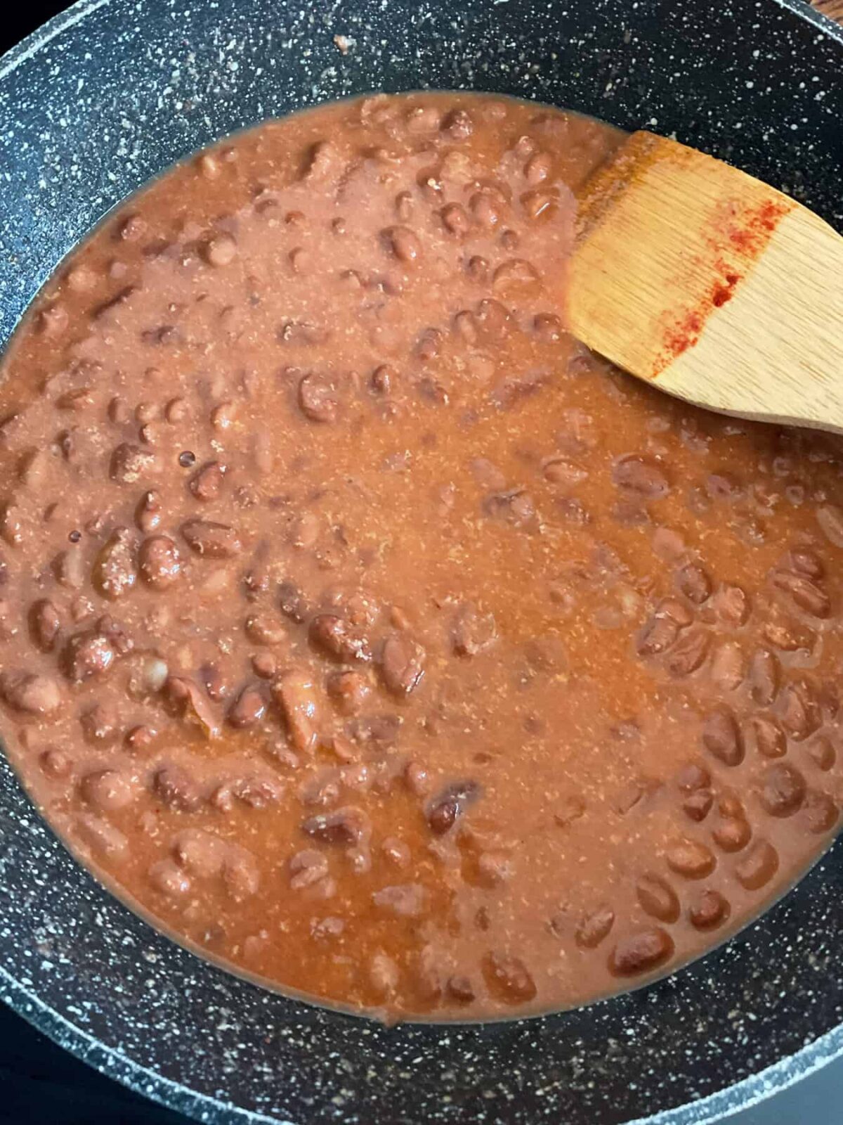 Refried bean ingredients mixed together in pan with wooden spatula.