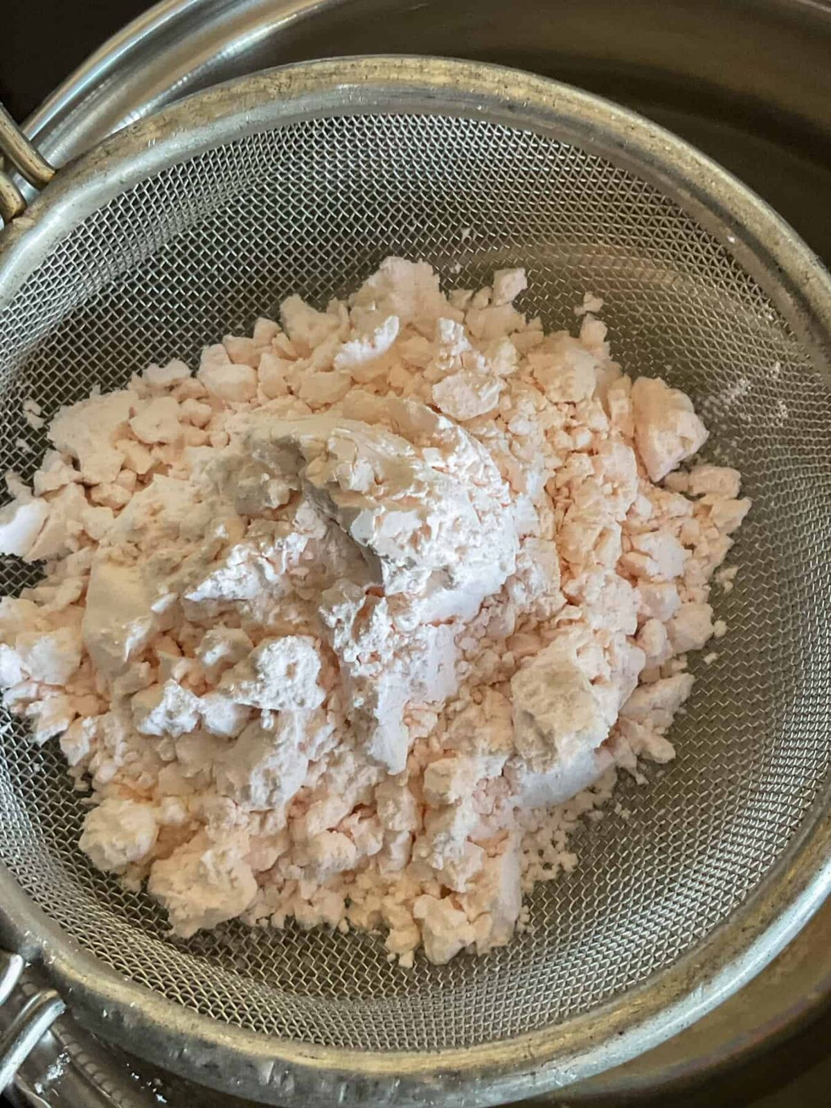 Custard powder in a sieve over a pan.