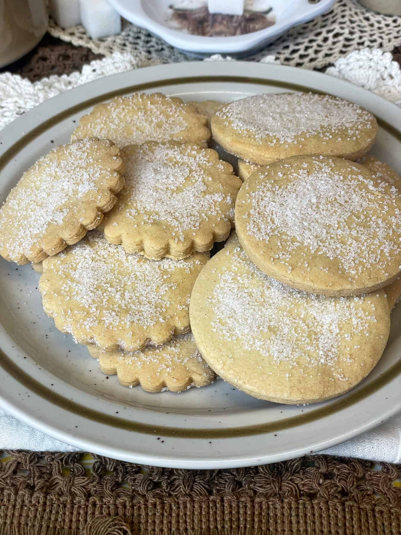 A brown rimmed plate with a pile of shortbread biscuits , brown and white table mats.