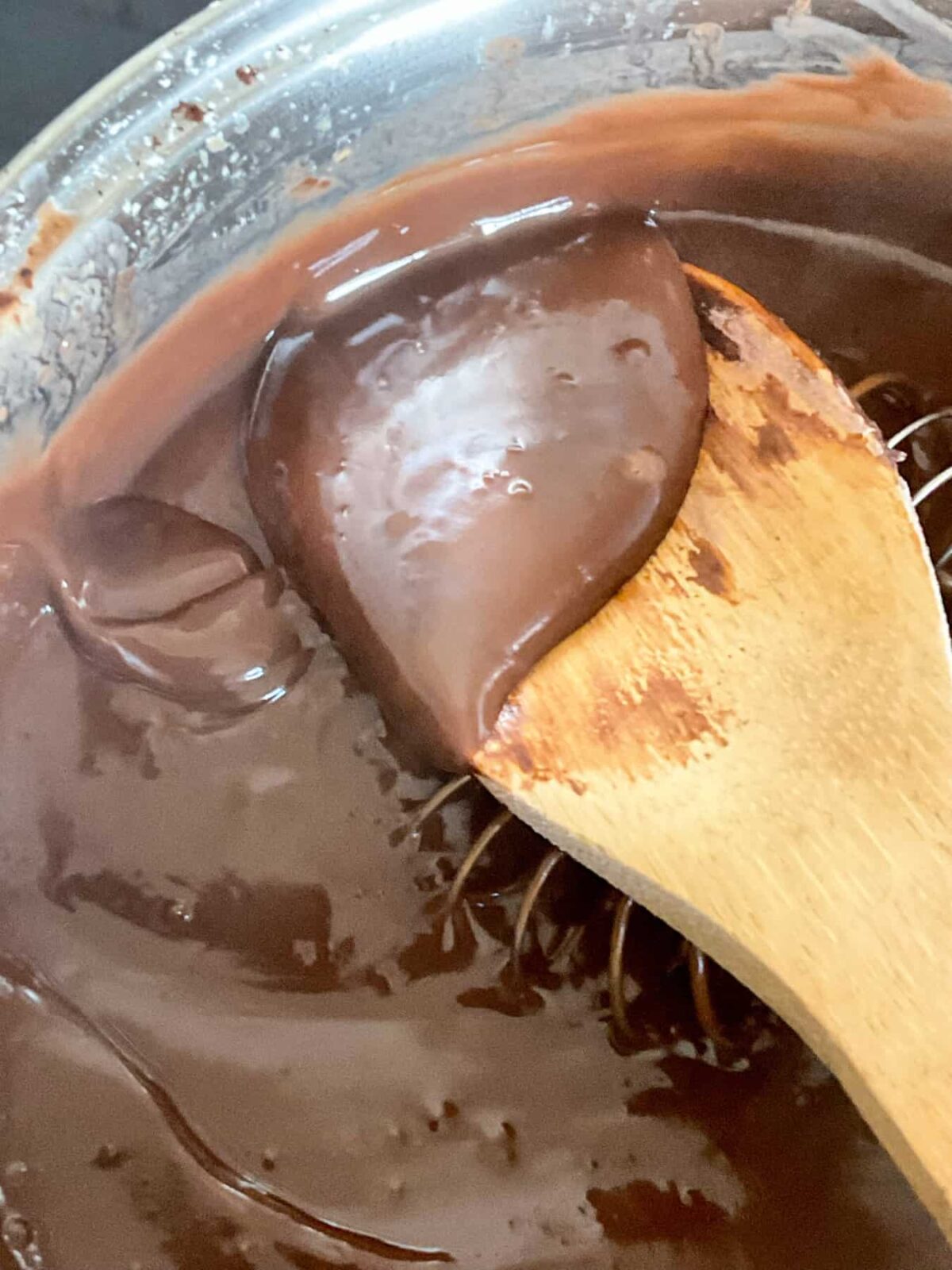 Chocolate custard pudding cooked and thick in the saucepan with wooden spoon lifting some pudding up.