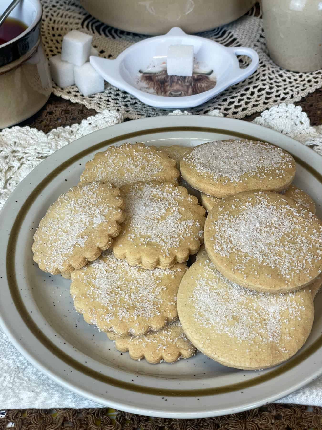 A plate of shortbread biscuits, tea pot in background with cup of tea and sugar cubes.