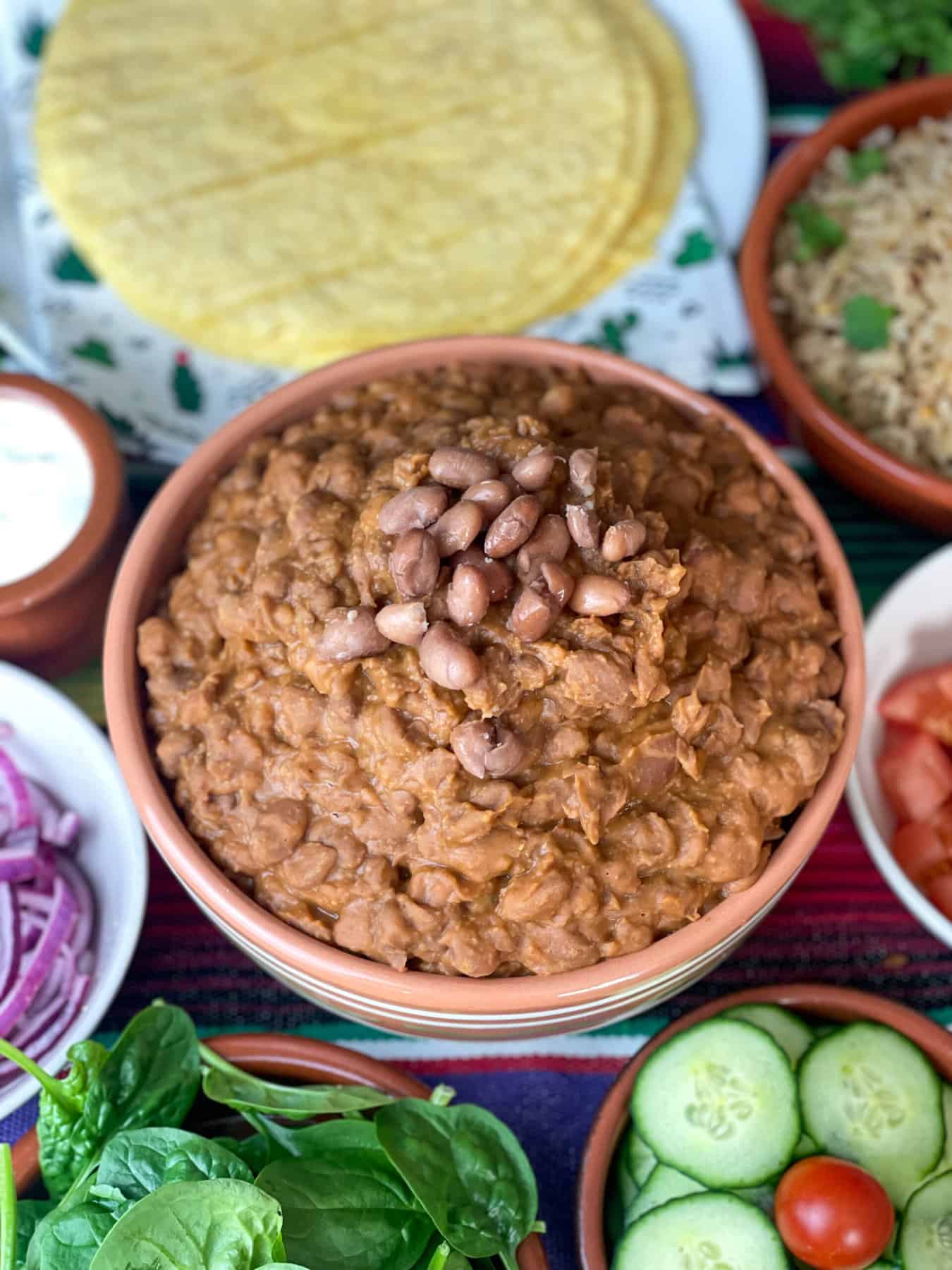Close up of refried beans on dinner table with lots of individual bowls of sides.