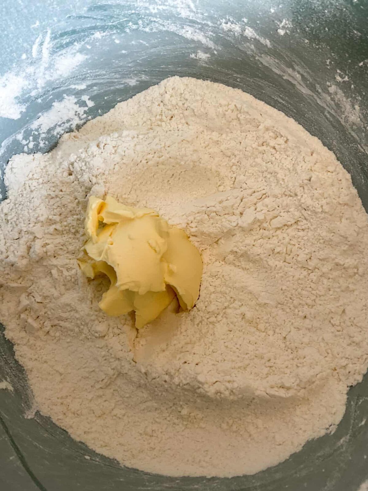 A blue mixing bowl with flour mixture and margarine, for scones.