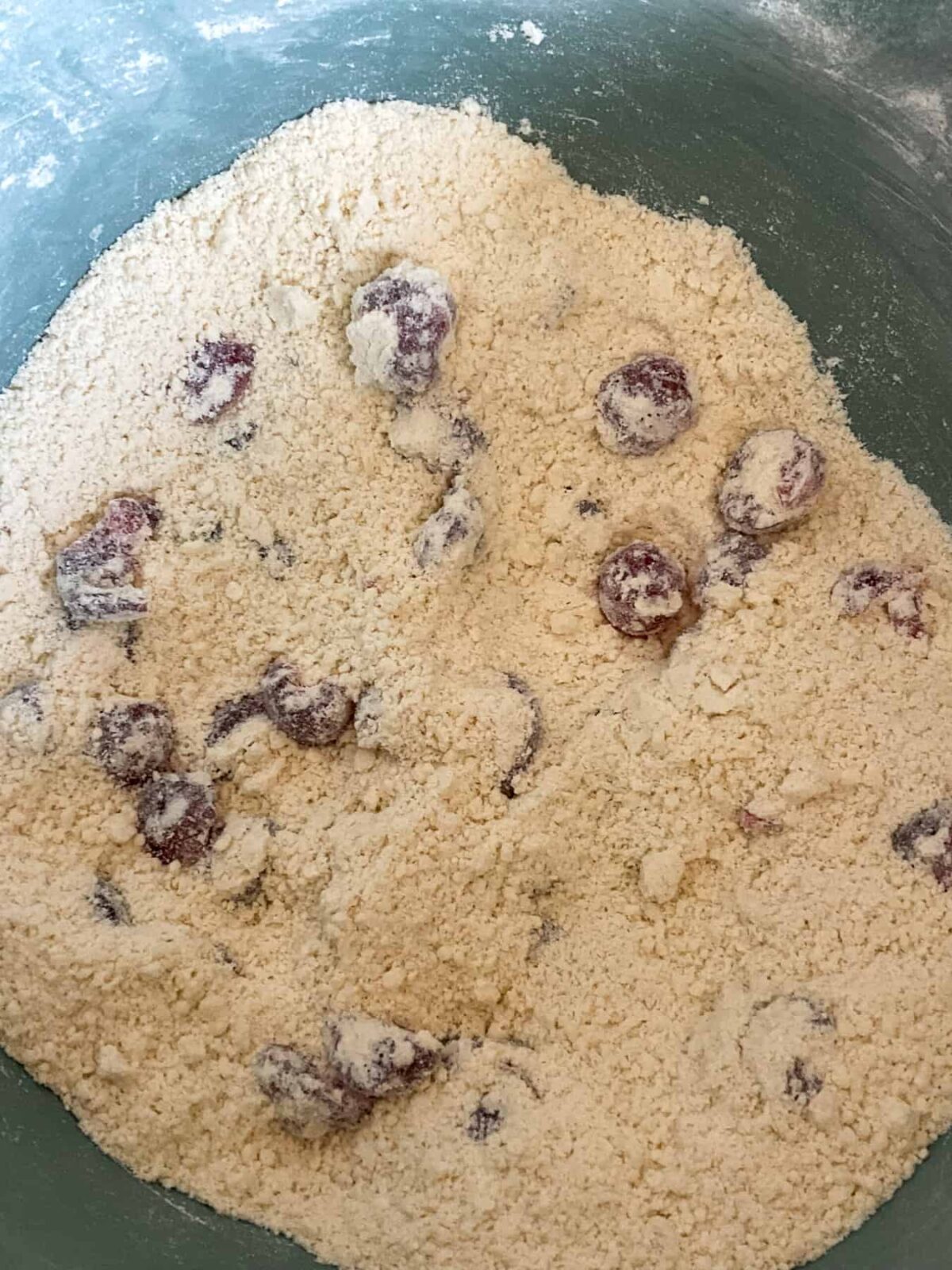 Glace cherries stirred through the crumbed scone mixture in mixing bowl.