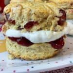 A close up of a cherry scone filled with jam and cream sitting on a spotty plate with pink mat underneath.