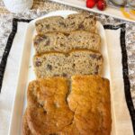 A tray with slices of banana chocolate chip bread and a ruffled table mat, strawberries to the side with a small dish of strawberry jam, featured image