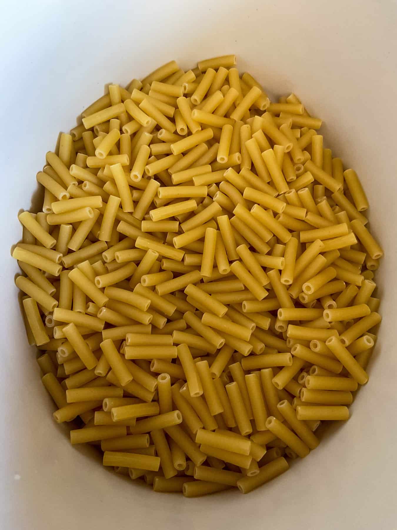 Macaroni pasta shapes in white slow cooker pot,