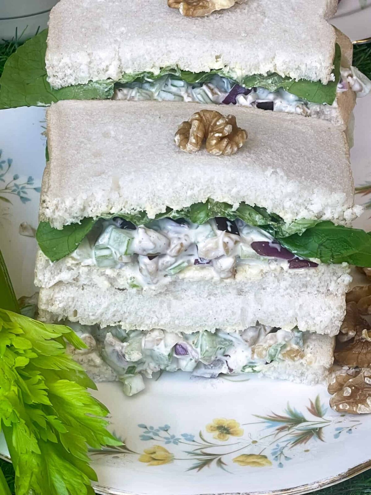 A stack of walnut celery sandwiches on yellow flower patterned plate with celery leaves to side.