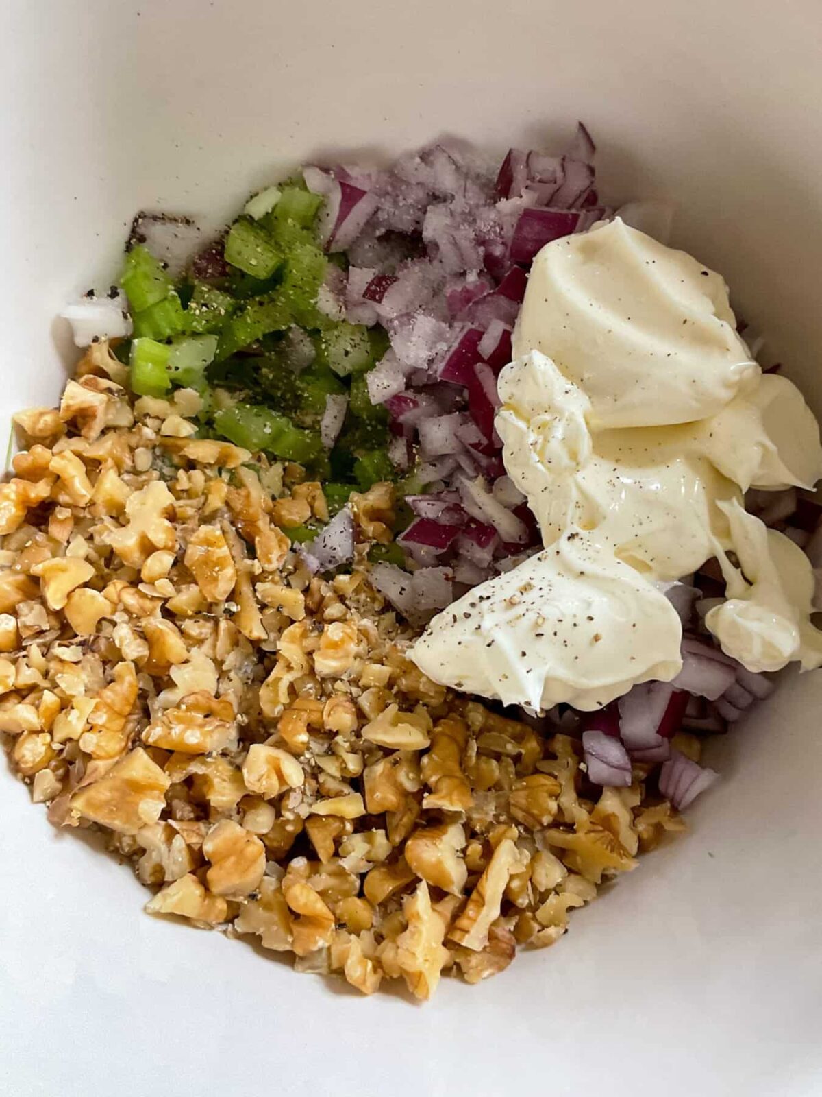 Vegan mayonnaise, salt and pepper added to diced veggies and walnuts in the mixing bowl.