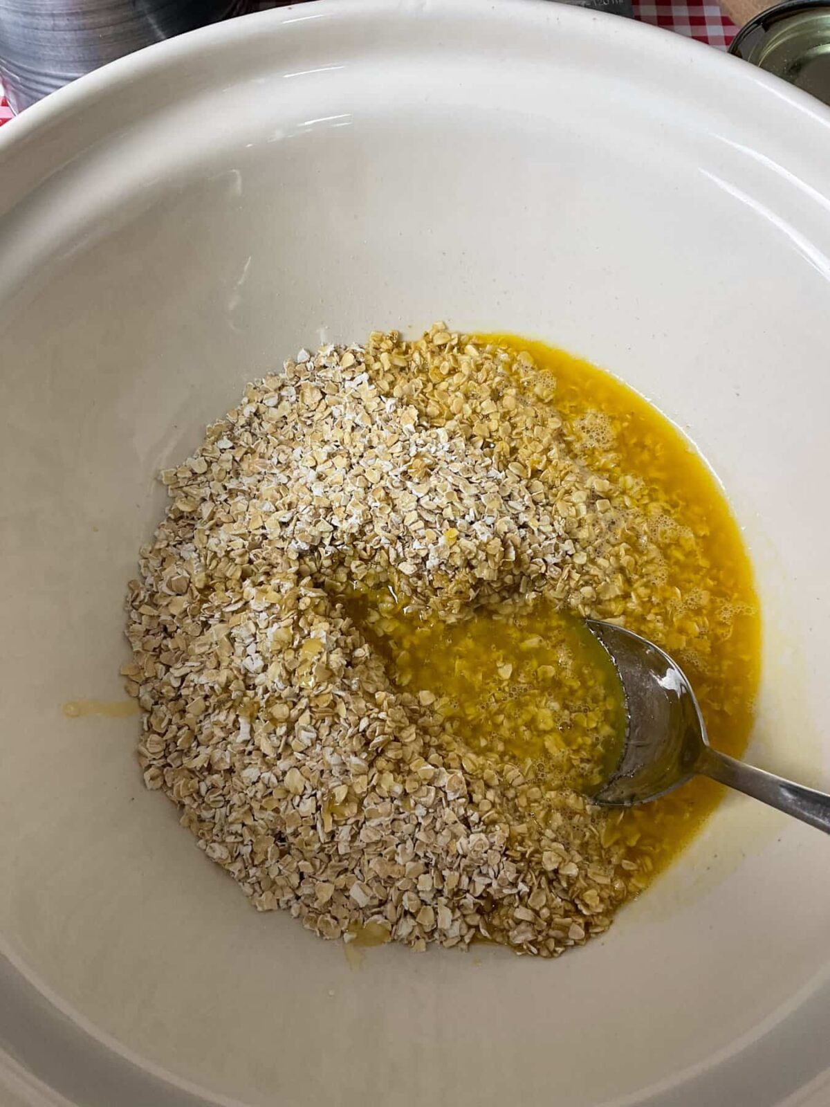 Melted ingredients poured over the oats in bowl with a silver spoon.