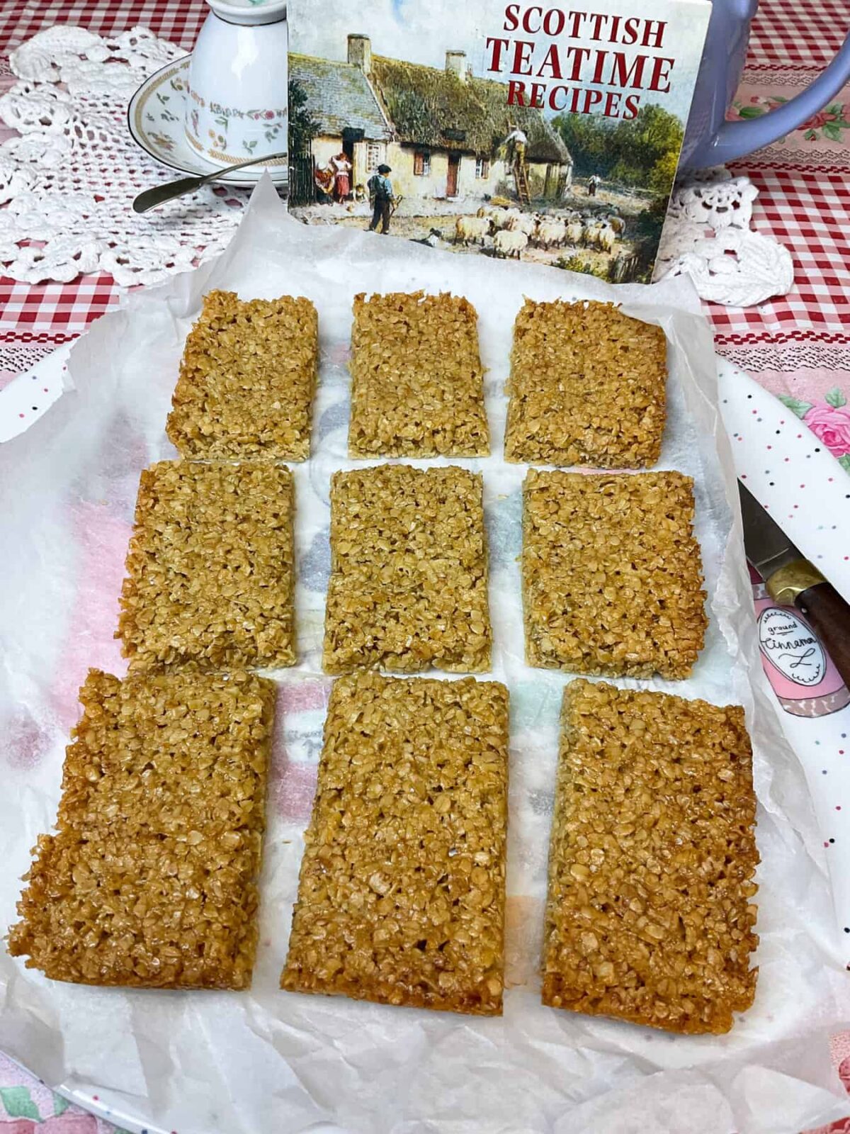 Flapjacks removed from the tin and still on baking paper, with Scottish teatime book in background.