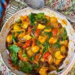 Vegan jalfrezi curry in Wok with silver vintage serving spoon to side, and colourful patterned table cloth background.