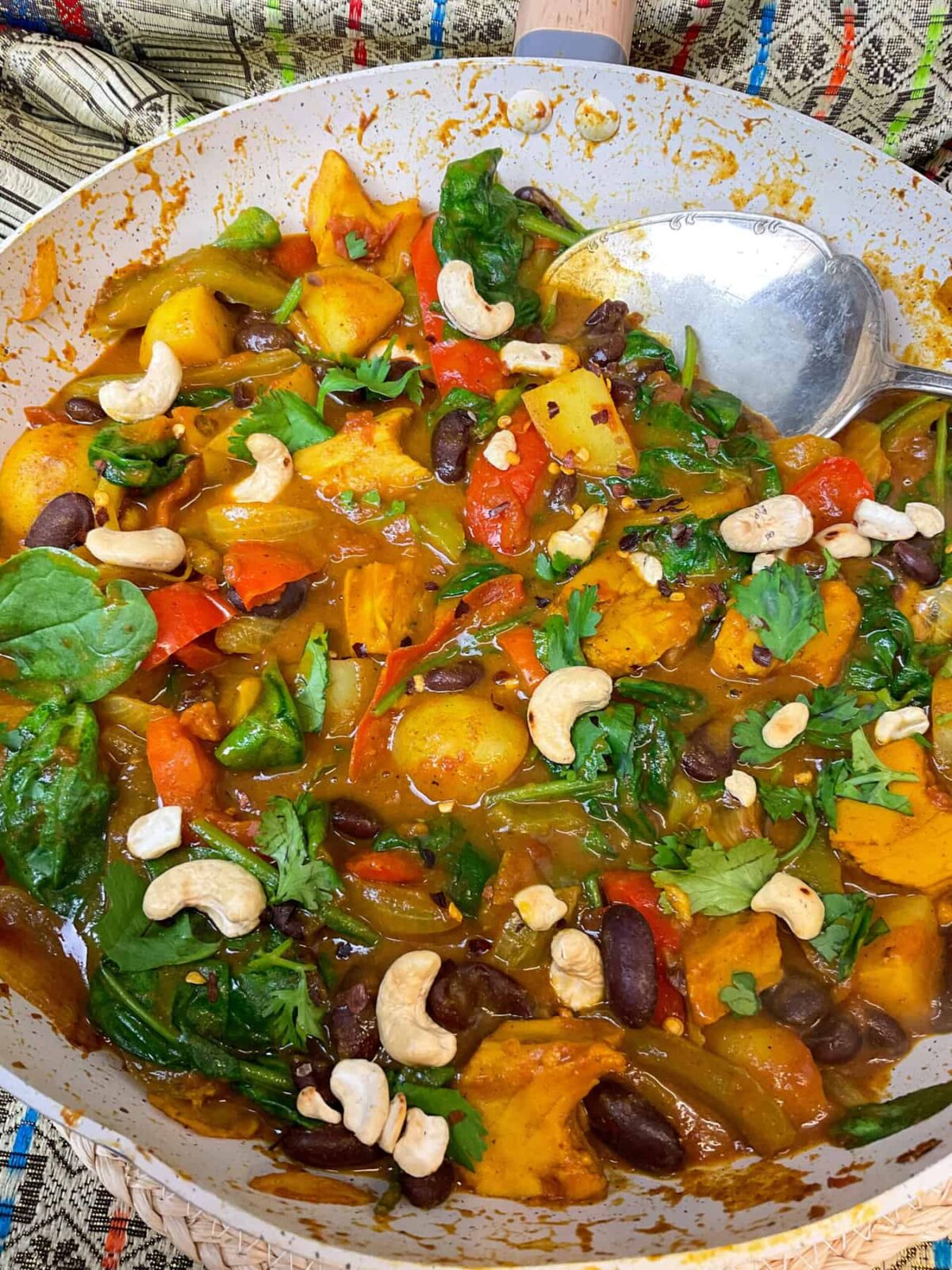 Vegan jalfrezi curry cooked and garnished with toasted cashews in the Wok with silver serving spoon to side.