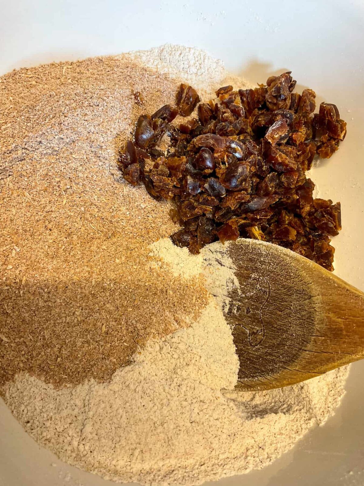 Dates and bran added to the mixing bowl with wooden spoon to mix.