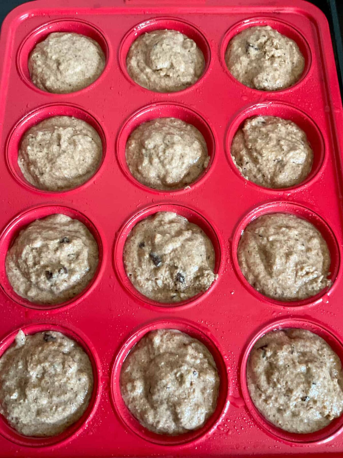 Choc chip bran muffin unbaked mixture in a red muffin tray,