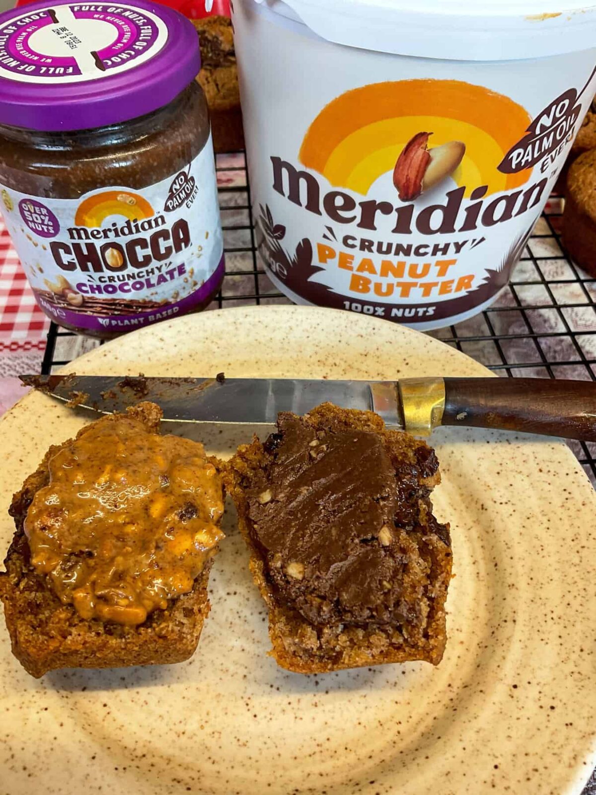 Two slices of muffin with one having peanut butter spread over and the second chocolate spread, chocolate spread jar in background with peanut butter tub.