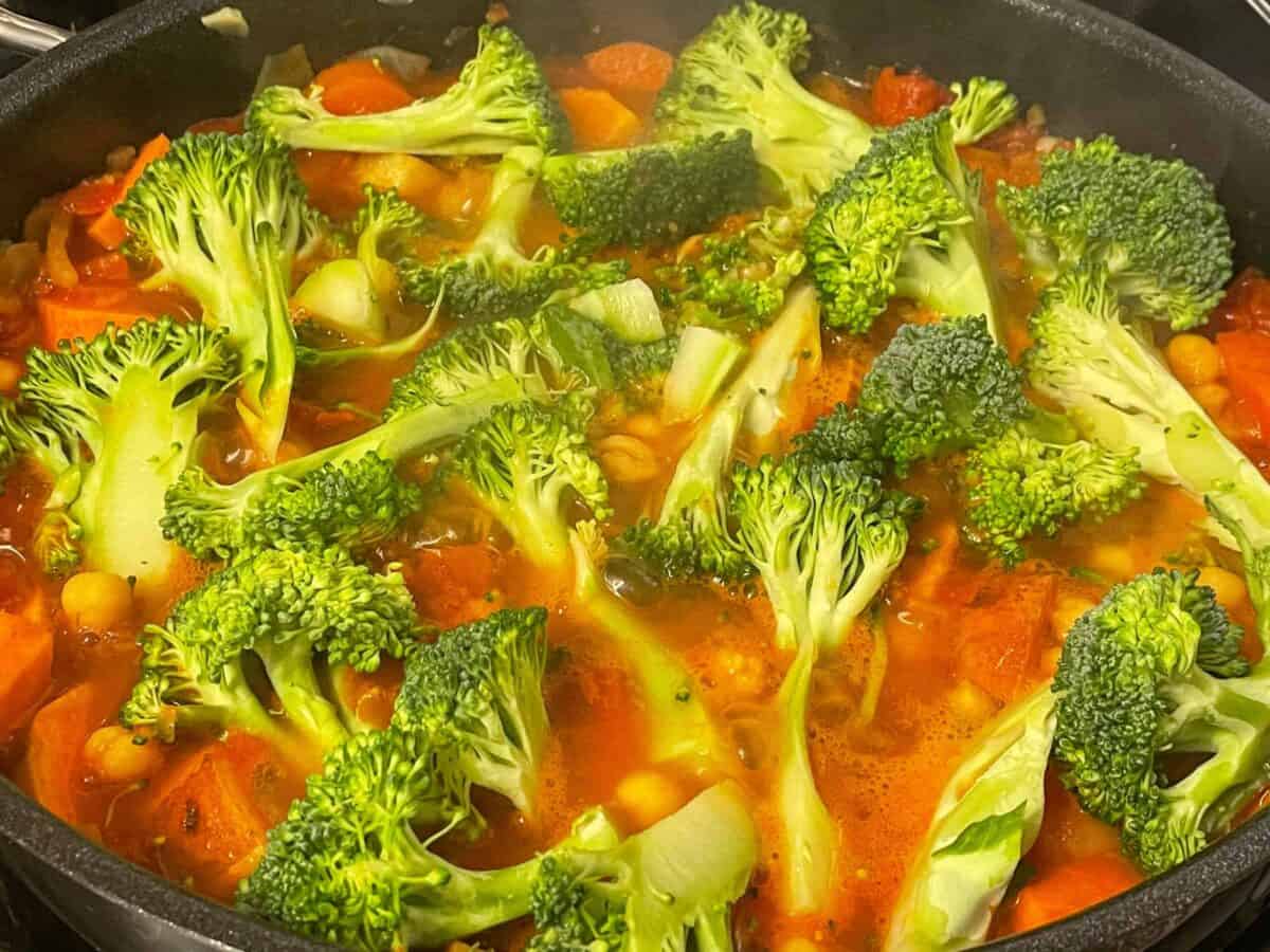 Broccoli added to red Thai curry cooking in pan.