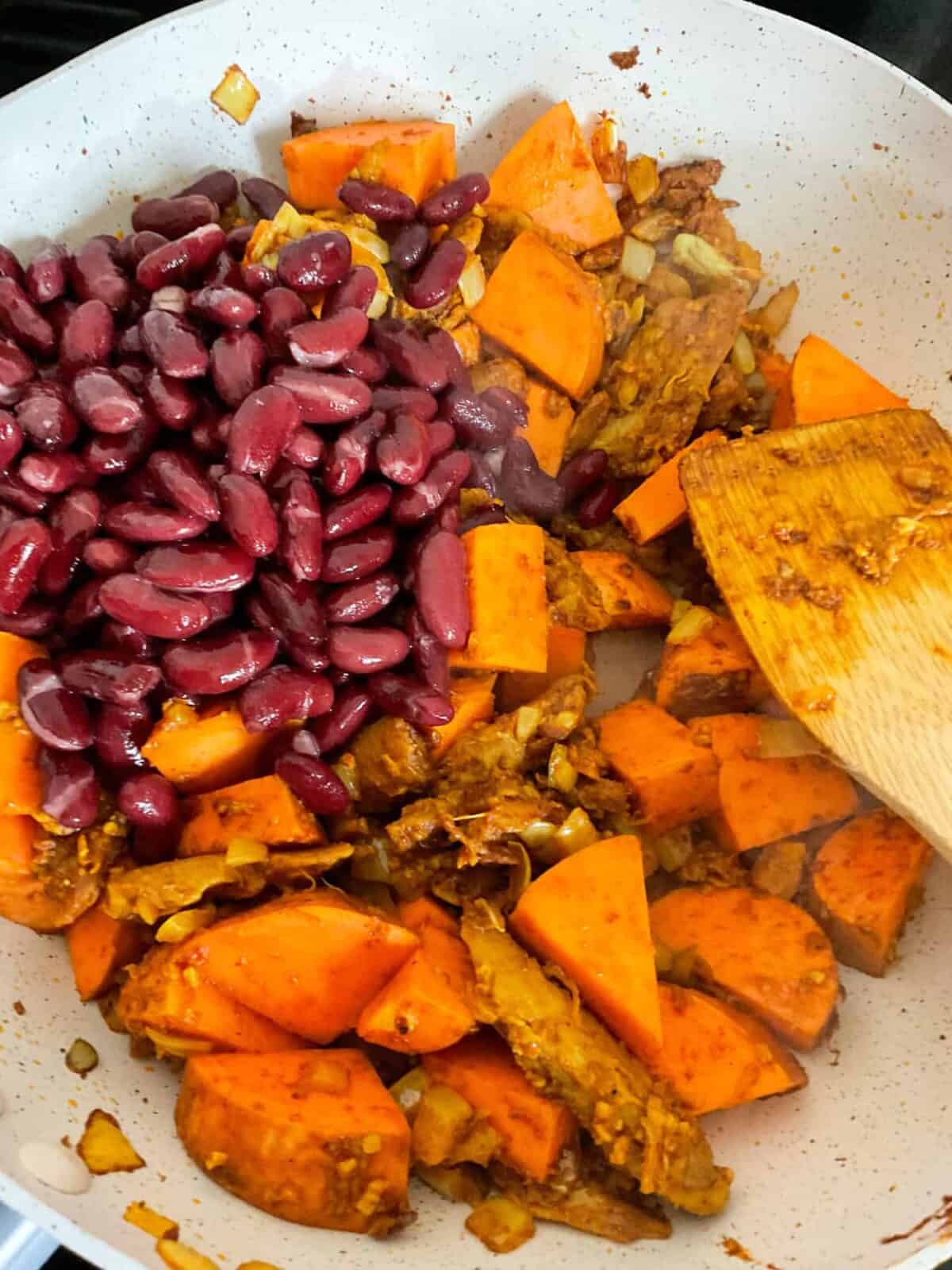 Sweet potato chunks and beans added to vindaloo cooking in pan.