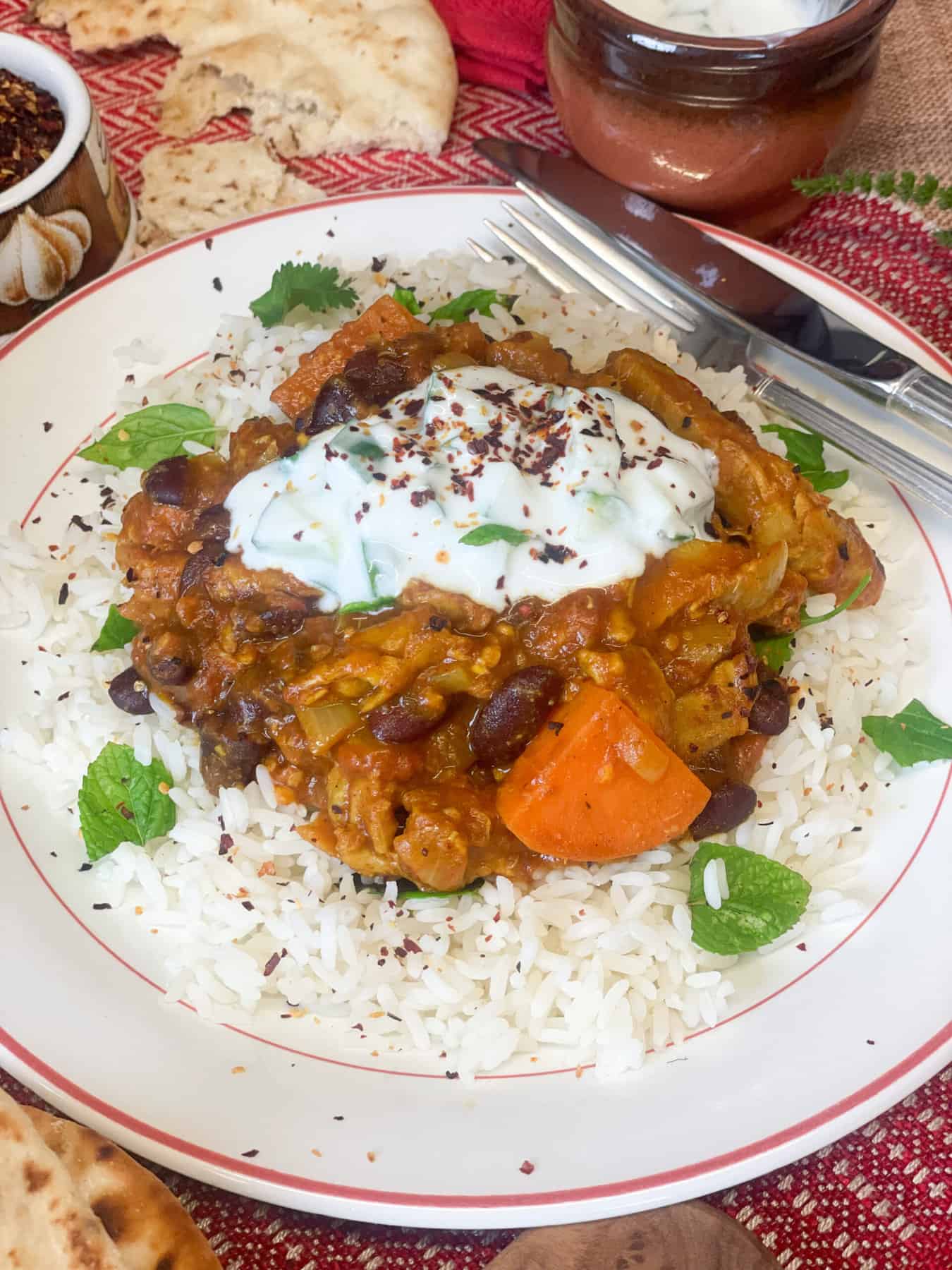 Close up of served curry and raita on plate with coriander garnish.