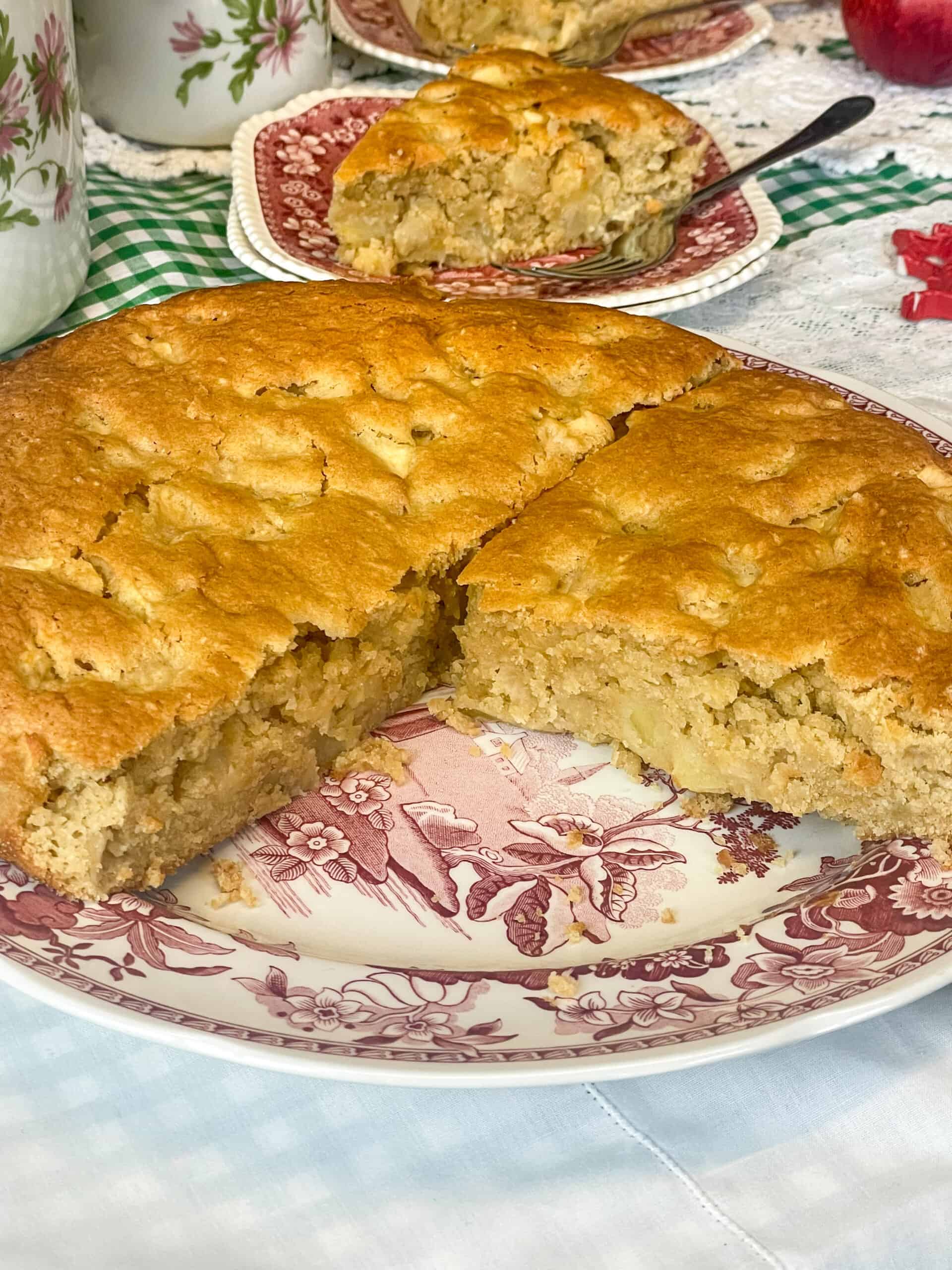 Apple cake with a large chunk removed, small slice in background.
