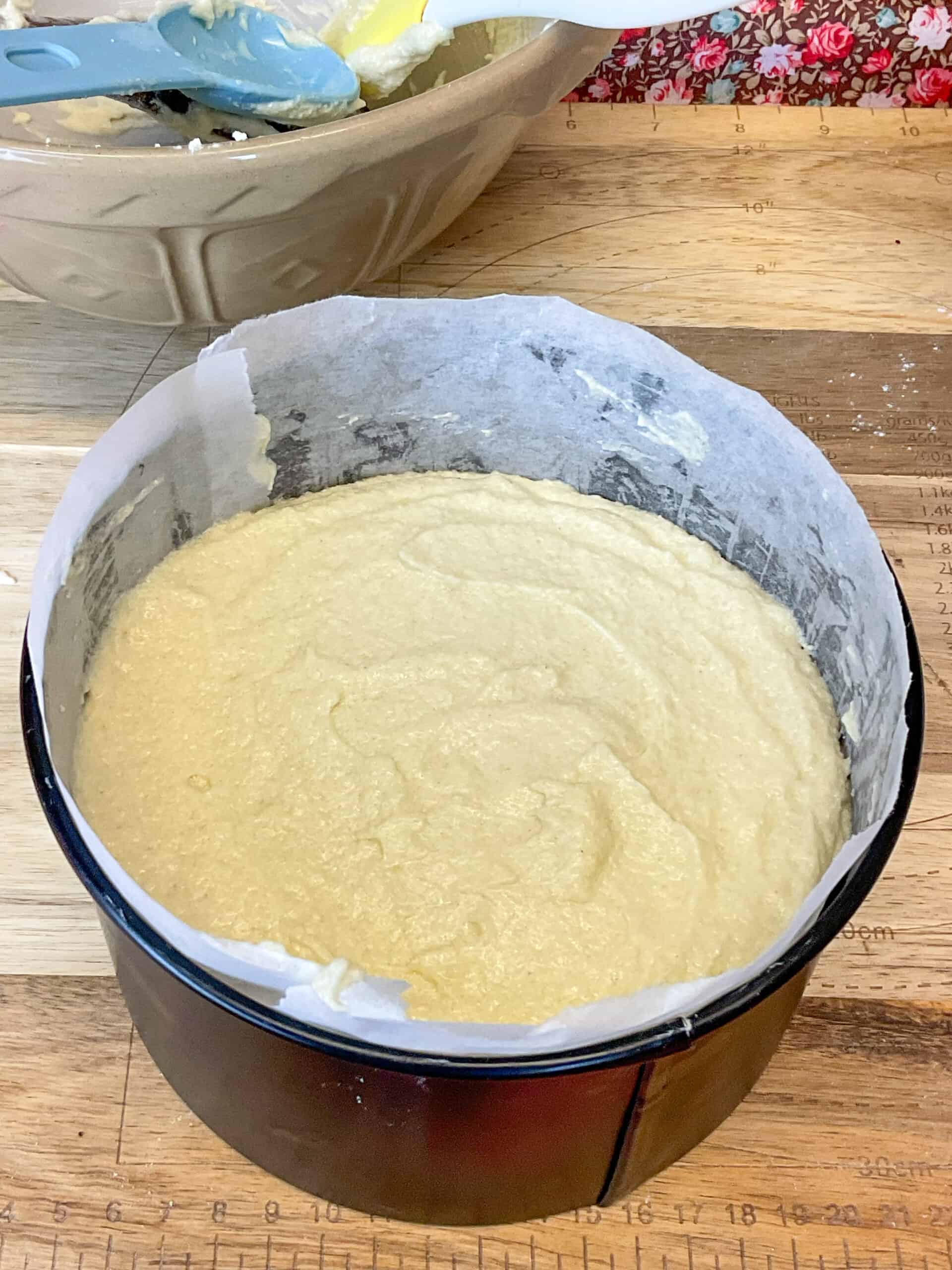 Ground rice cake mixture added to cake tin with mixing bowl to side.
