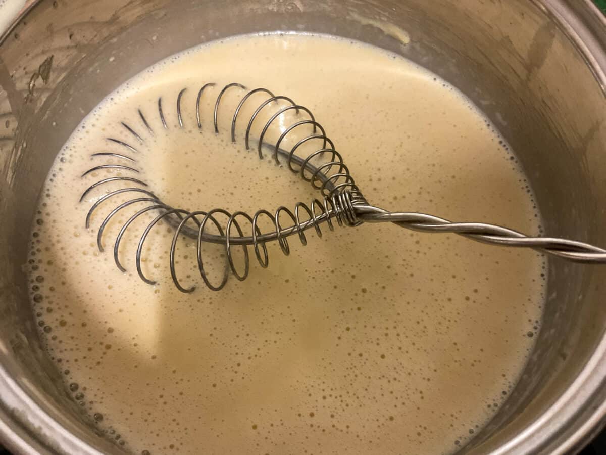 Milk poured into flour and butter mix in saucepan and whisked with wire whisk.
