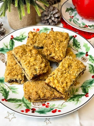 A festive patterned plate with mincemeat crumble traybake bars on top and small hessian plant pot to side.