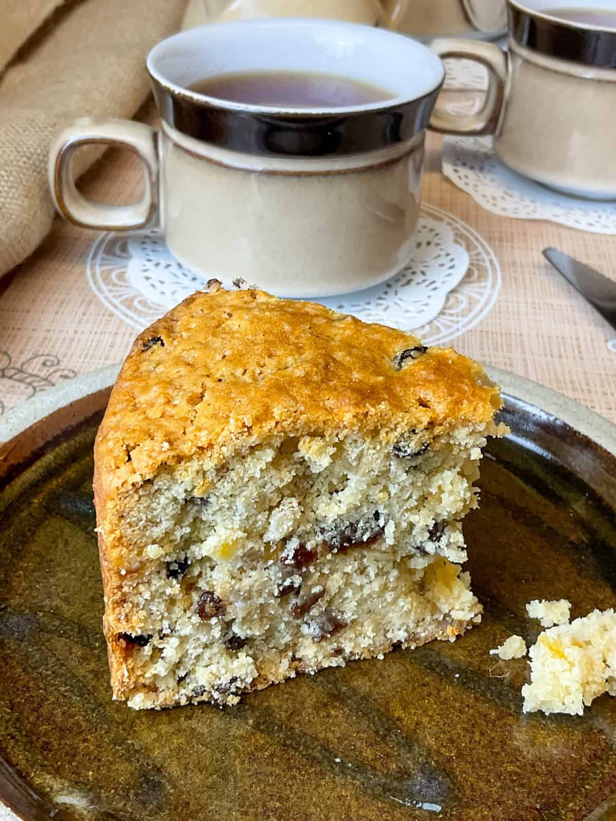 A slice of fruit cake on a brown plate with cup of tea.
