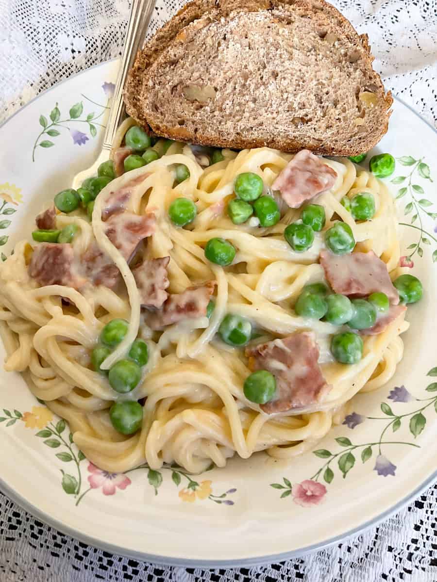 Vegan Spaghetti Carbonara served on flower patterned plate with bread to side, and white tablecloth.