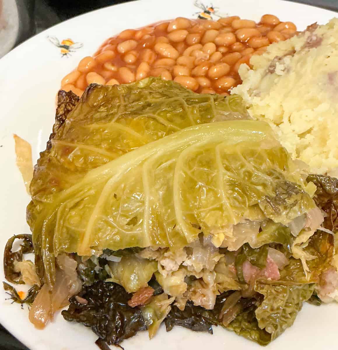 Baked cabbage layer served on plate with mashed potatoes and baked beans.