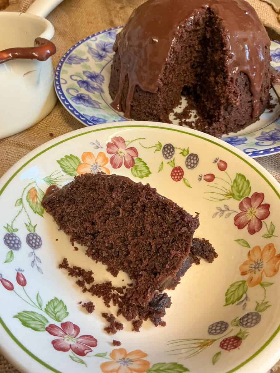 A slice of chocolate pudding on serving bowl with chocolate pudding in background.