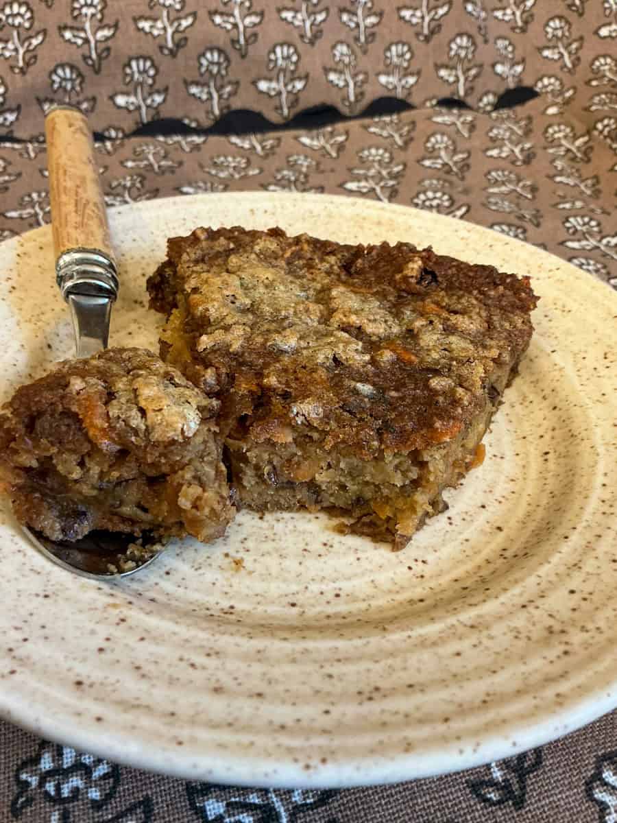 Slice of Duke pudding on small serving plate with wooden handled dessert spoon.
