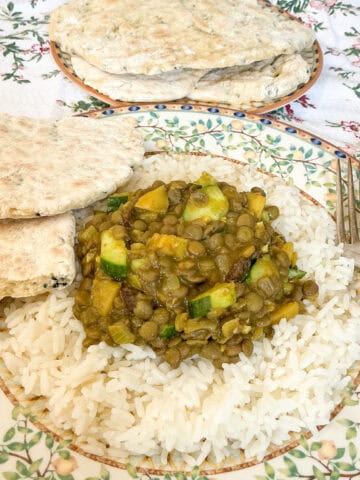 Featured image for lentil curry, served on a plate with flatbreads to side.