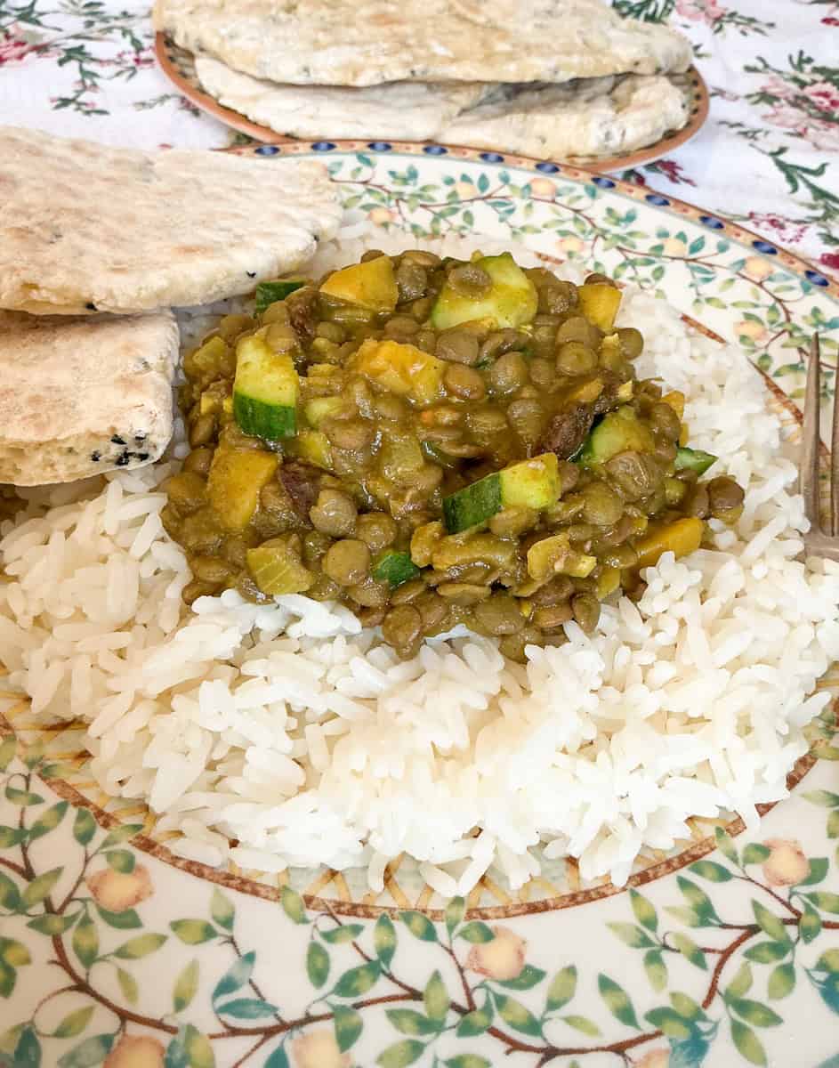 A plate with old-fashioned lentil curry served with rice and flatbreads, more flatbreads on plate in background.