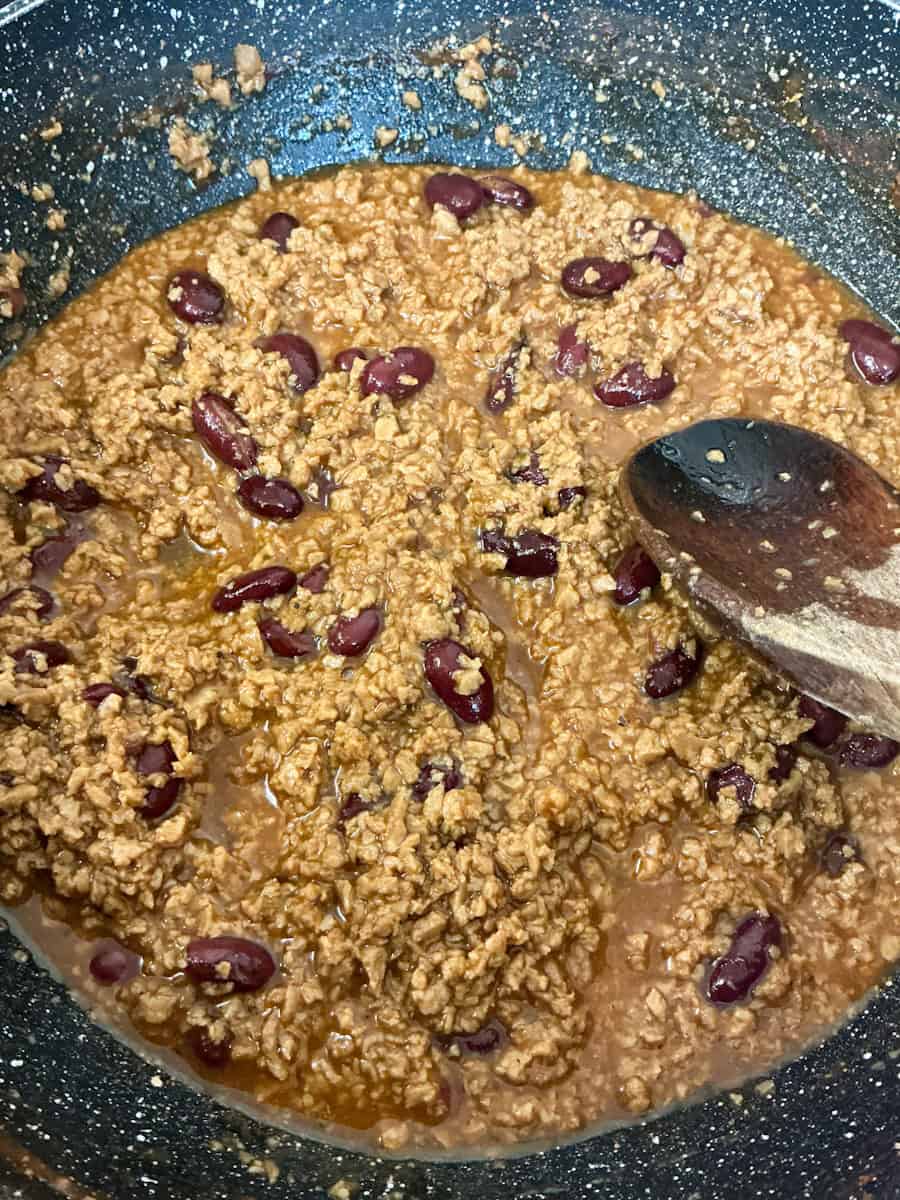 Kidney beans added to pan and stirred with wooden spoon.
