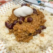 Close up of beanfeast chilli served with coucous and a scoop of mayonnaise, cutlery to side.