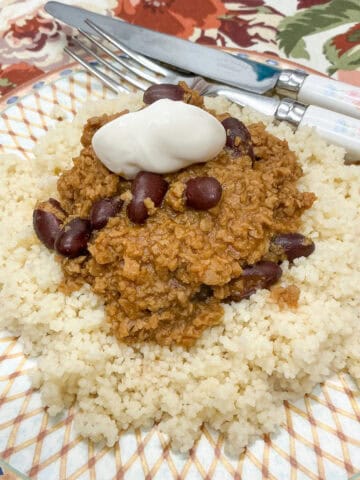 Close up of beanfeast chilli served with coucous and a scoop of mayonnaise, cutlery to side.