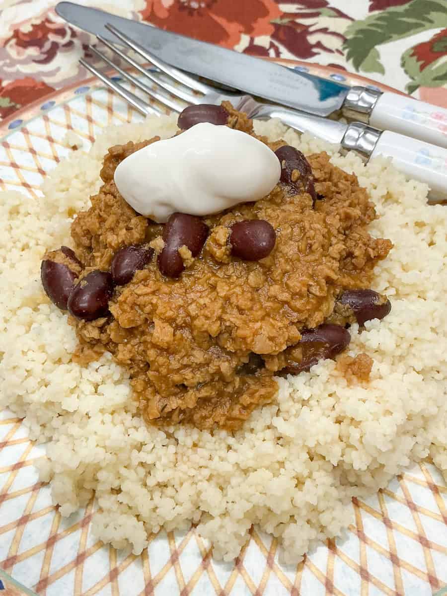 Close up of beanfeast chilli served with coucous and a scoop of mayonnaise, cutlery to side.